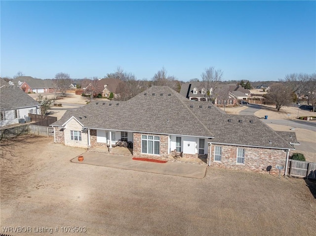 view of front of house with stone siding, a residential view, roof with shingles, and fence