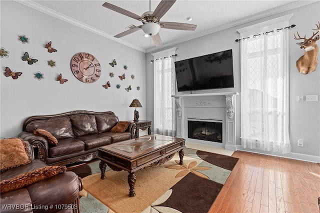 living room with a fireplace with flush hearth, a ceiling fan, wood-type flooring, crown molding, and baseboards