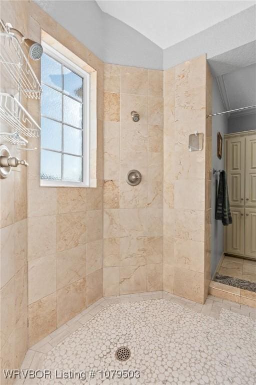 bathroom with a tile shower and lofted ceiling