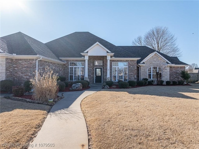 view of front of house with stone siding, a shingled roof, and a front lawn