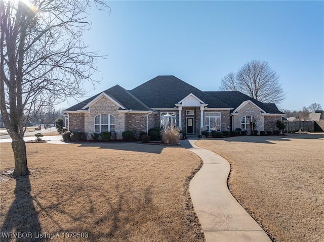 view of front of property featuring stone siding, roof with shingles, and a front lawn