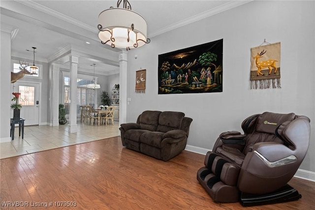 living area with hardwood / wood-style floors, an inviting chandelier, crown molding, baseboards, and ornate columns