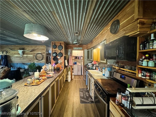 kitchen with wooden walls, sink, washer and dryer, hardwood / wood-style floors, and stainless steel stove