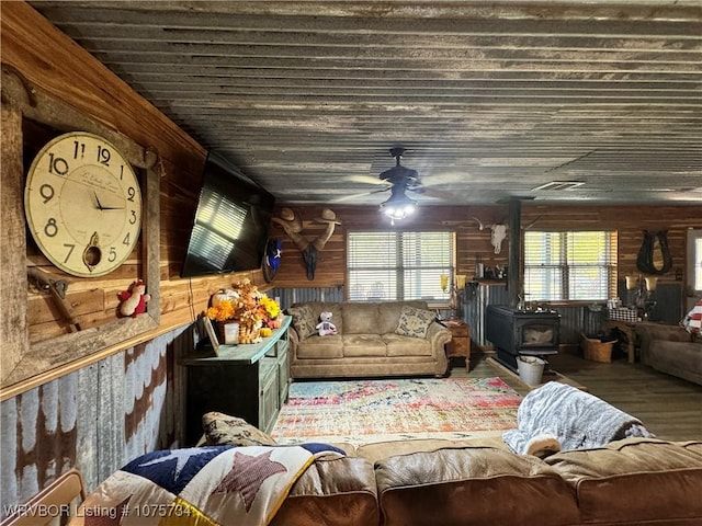 living room featuring a wood stove, ceiling fan, wooden ceiling, and a wealth of natural light