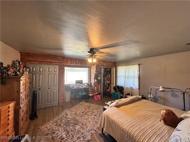 bedroom featuring wood-type flooring, a textured ceiling, ceiling fan, and wooden walls