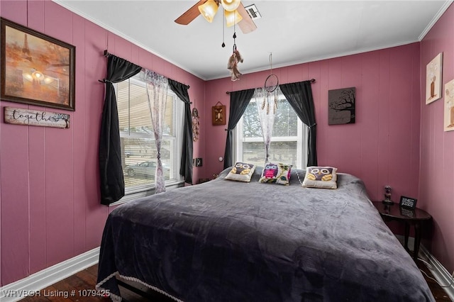 bedroom featuring visible vents, crown molding, baseboards, wood finished floors, and a ceiling fan