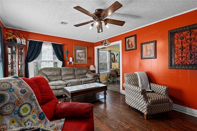 living area featuring wood finished floors, visible vents, ornamental molding, ceiling fan, and a textured ceiling