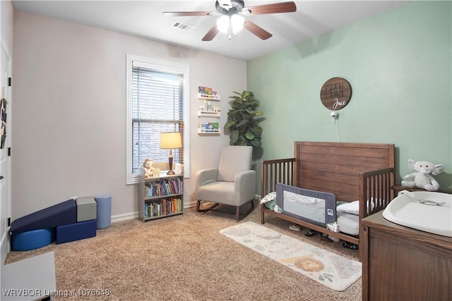 carpeted bedroom featuring a crib and ceiling fan