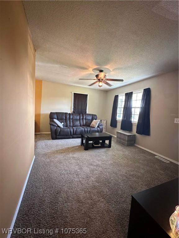 living room with ceiling fan, carpet floors, and a textured ceiling