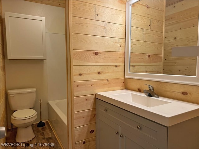 bathroom featuring toilet, wood walls, wood-type flooring, vanity, and a bath