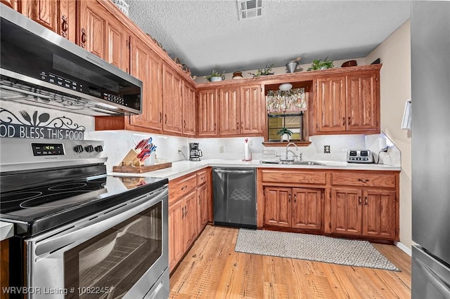 309 Neal Dr, Roland, OK 74954 - kitchen featuring stainless steel appliances, light wood finished floors, light countertops, a textured ceiling, and brown cabinets