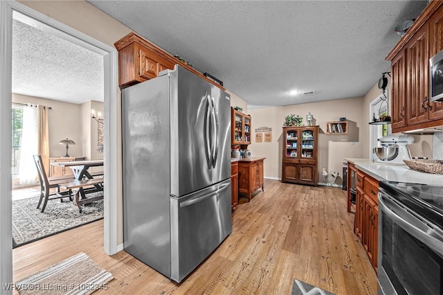 309 Neal Dr, Roland, OK 74954 - kitchen with appliances with stainless steel finishes, a textured ceiling, light wood finished floors, brown cabinetry, and light countertops