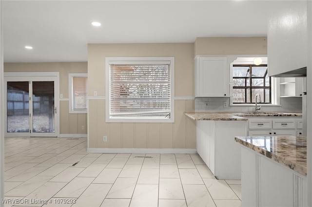 kitchen with tasteful backsplash, light stone counters, white cabinetry, a sink, and recessed lighting