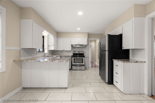 kitchen with a peninsula, under cabinet range hood, appliances with stainless steel finishes, and light stone countertops