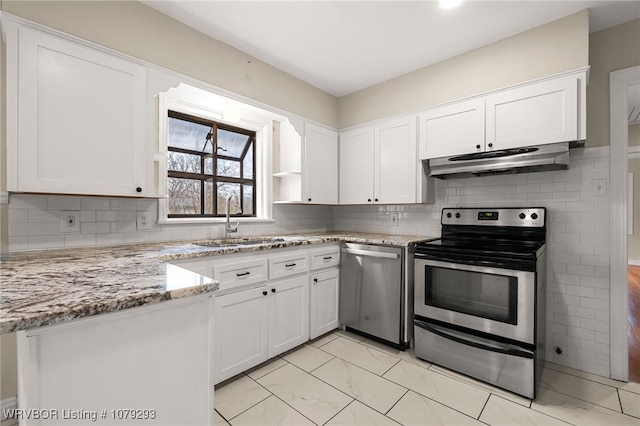 kitchen featuring light stone counters, under cabinet range hood, stainless steel appliances, a sink, and white cabinets