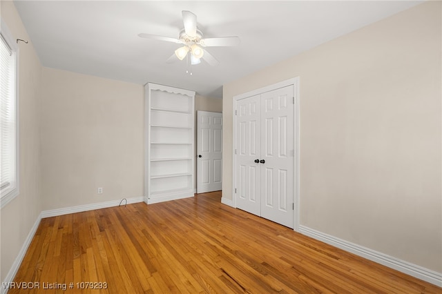 unfurnished bedroom with light wood-type flooring, multiple windows, baseboards, and two closets