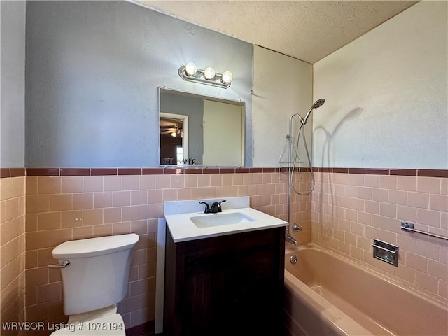 full bathroom featuring vanity, washtub / shower combination, toilet, a textured ceiling, and tile walls