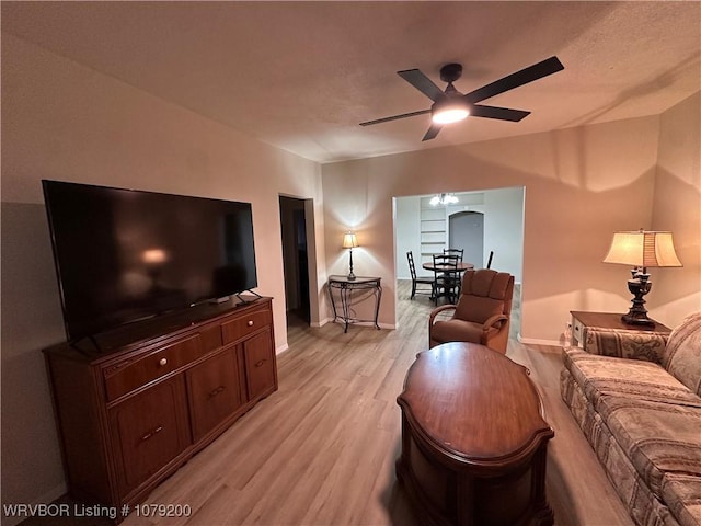 living area featuring arched walkways, ceiling fan, light wood-style flooring, and baseboards