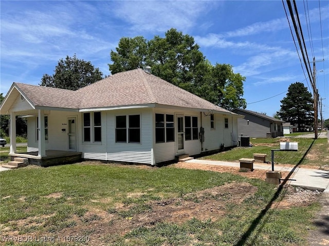 view of front facade with a porch, cooling unit, roof with shingles, and a front lawn