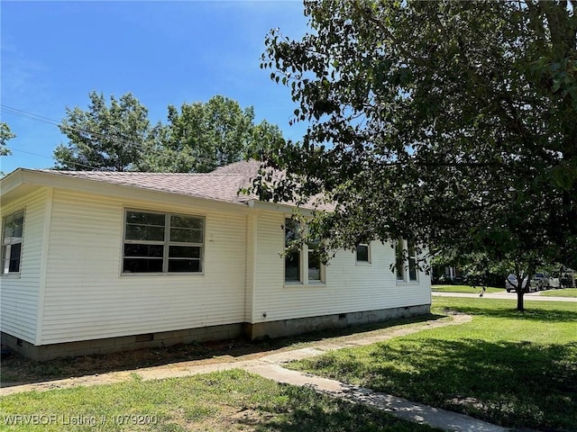 view of side of home featuring crawl space, roof with shingles, and a yard