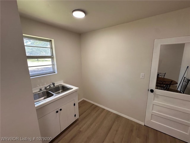 kitchen featuring light wood finished floors, baseboards, white cabinets, light countertops, and a sink