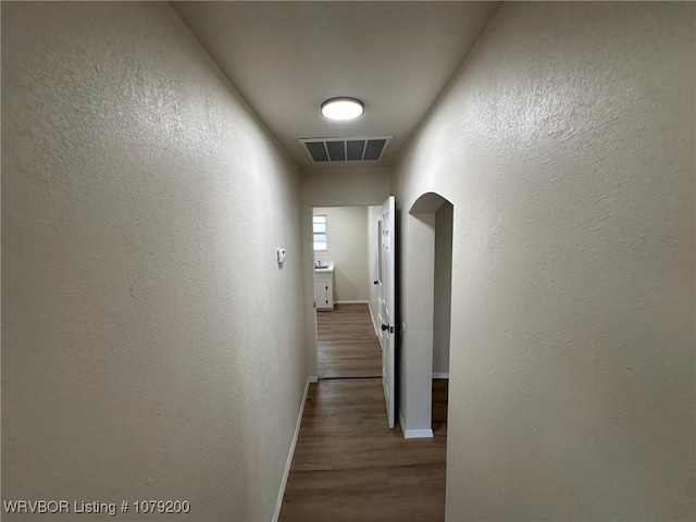 hall with visible vents, arched walkways, dark wood-style flooring, and a textured wall