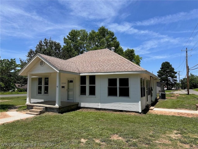 bungalow-style house featuring central AC, a porch, roof with shingles, and a front yard