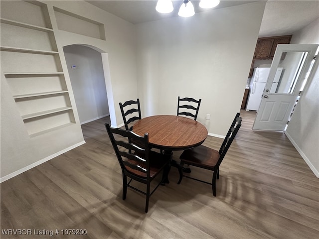 dining room featuring built in features, arched walkways, baseboards, and wood finished floors