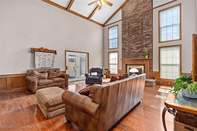 living area featuring a wainscoted wall, a ceiling fan, a brick fireplace, high vaulted ceiling, and hardwood / wood-style floors