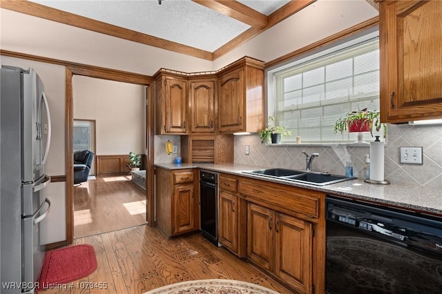 kitchen with a sink, light wood-style floors, black dishwasher, freestanding refrigerator, and brown cabinets