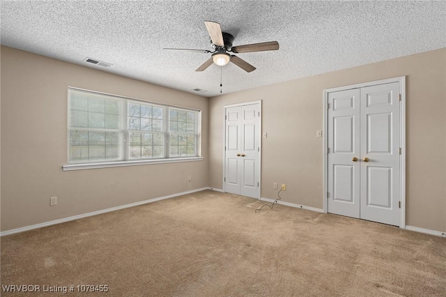 unfurnished bedroom featuring carpet, multiple closets, visible vents, a textured ceiling, and baseboards