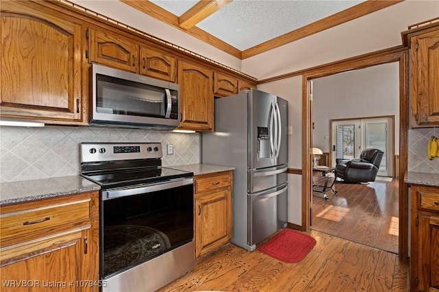 kitchen with stainless steel appliances, brown cabinets, light wood-style floors, and decorative backsplash