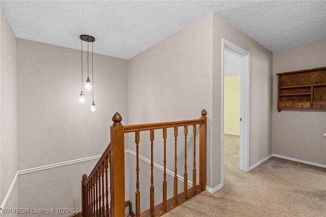 hallway featuring carpet, baseboards, a textured ceiling, and an upstairs landing