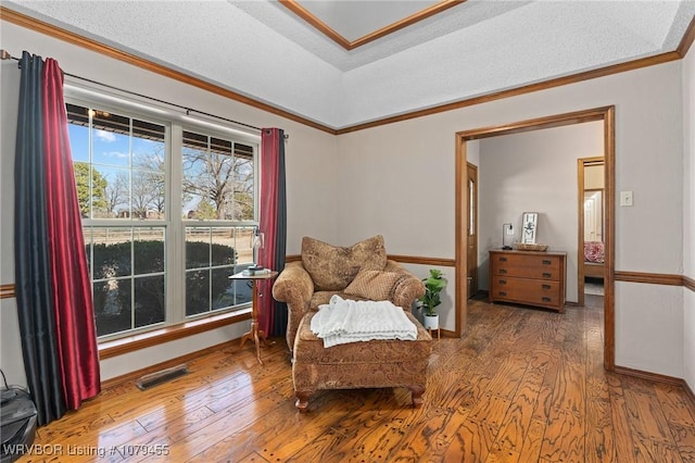 sitting room featuring baseboards, wood-type flooring, visible vents, and crown molding