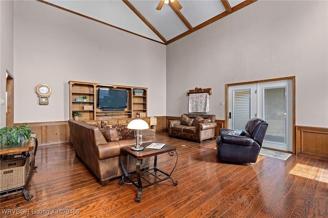 living area with ceiling fan, high vaulted ceiling, wood finished floors, and wainscoting