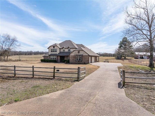 view of front of property with driveway, a fenced front yard, an attached garage, and a rural view