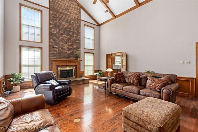 living room featuring a brick fireplace, a healthy amount of sunlight, wainscoting, and hardwood / wood-style flooring