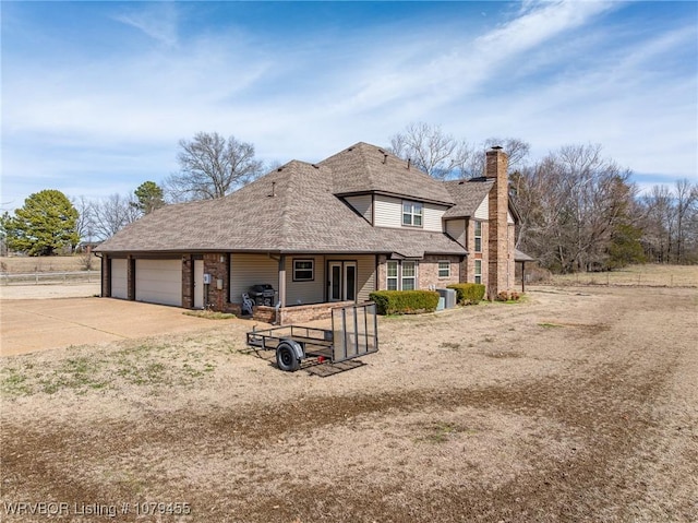 view of front facade with concrete driveway, a shingled roof, a chimney, and an attached garage