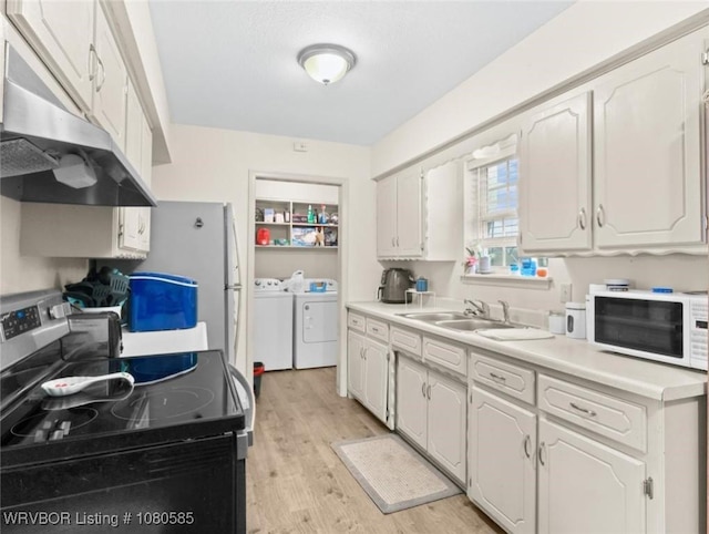 kitchen with a sink, under cabinet range hood, washer and clothes dryer, light wood finished floors, and white appliances