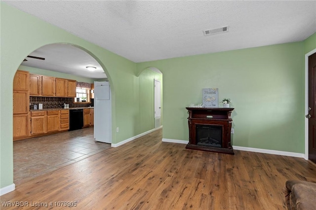 unfurnished living room featuring visible vents, arched walkways, wood finished floors, and a fireplace