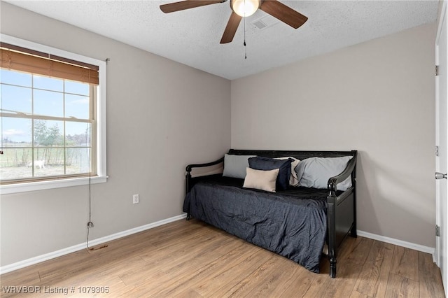 bedroom featuring a textured ceiling, light wood-type flooring, baseboards, and a ceiling fan