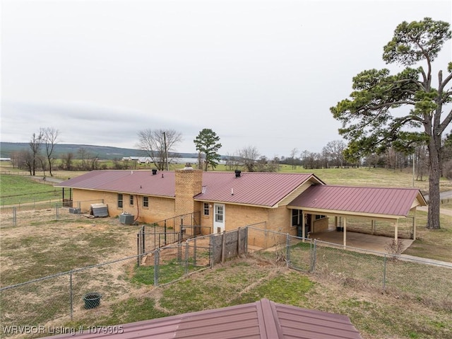 rear view of house with a rural view, an attached carport, central AC unit, and metal roof