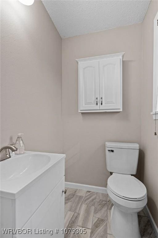 bathroom featuring a textured ceiling, toilet, vanity, and baseboards