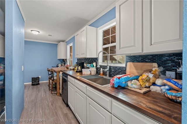 kitchen featuring wood counters, sink, white cabinetry, dishwashing machine, and light hardwood / wood-style floors