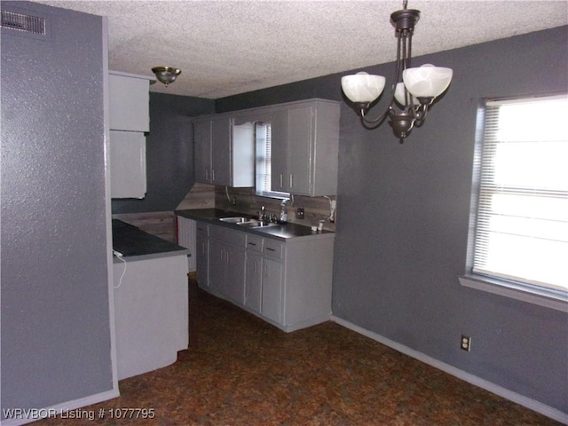 kitchen with sink, a notable chandelier, a textured ceiling, decorative light fixtures, and white cabinets