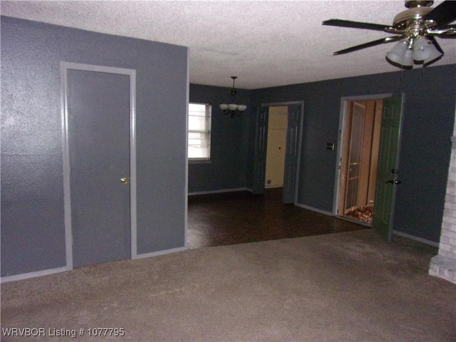 empty room featuring a textured ceiling, dark carpet, and ceiling fan with notable chandelier