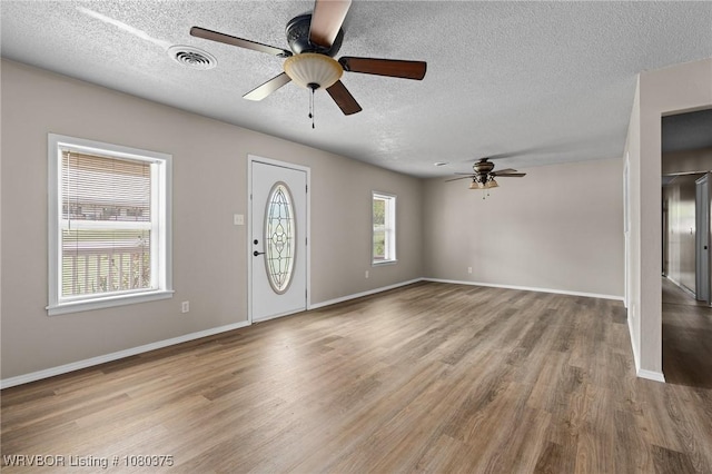 foyer entrance featuring wood finished floors, visible vents, a ceiling fan, baseboards, and a textured ceiling