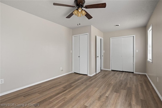 unfurnished bedroom with multiple closets, wood finished floors, visible vents, baseboards, and ceiling fan