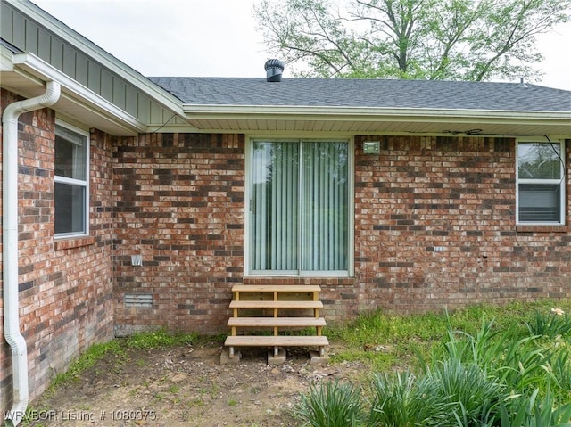 view of exterior entry featuring a shingled roof and brick siding