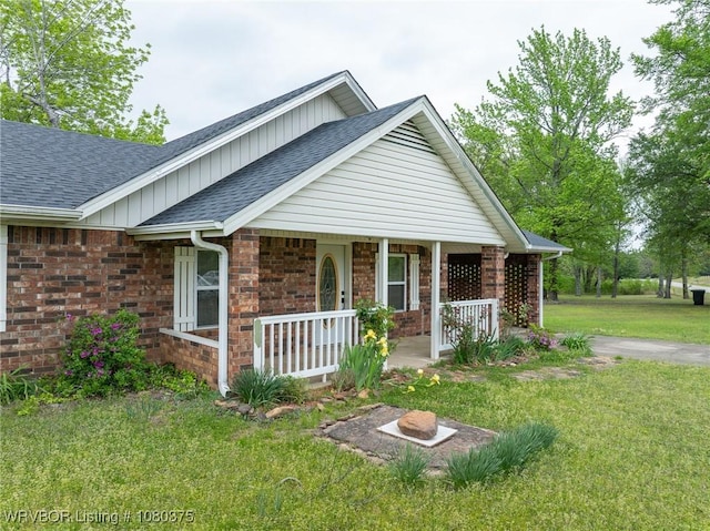 view of front of house featuring roof with shingles, covered porch, brick siding, board and batten siding, and a front yard